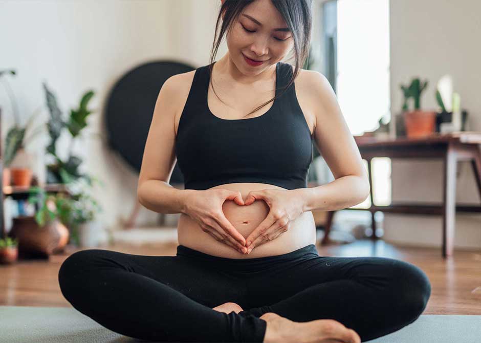A pregnant woman on a yoga mat making a heart with her own hands over her belly