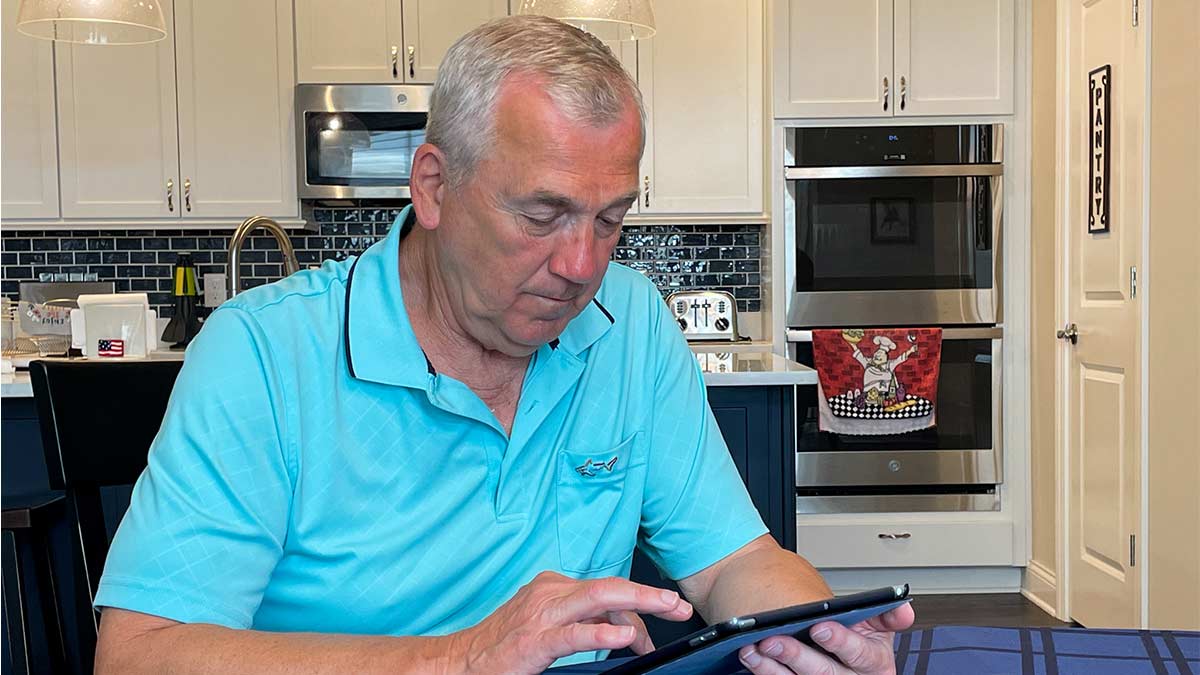 An older man using his tablet to take a self-administered Gerocognitive exam to test for early-stage Alzheimer's disease.