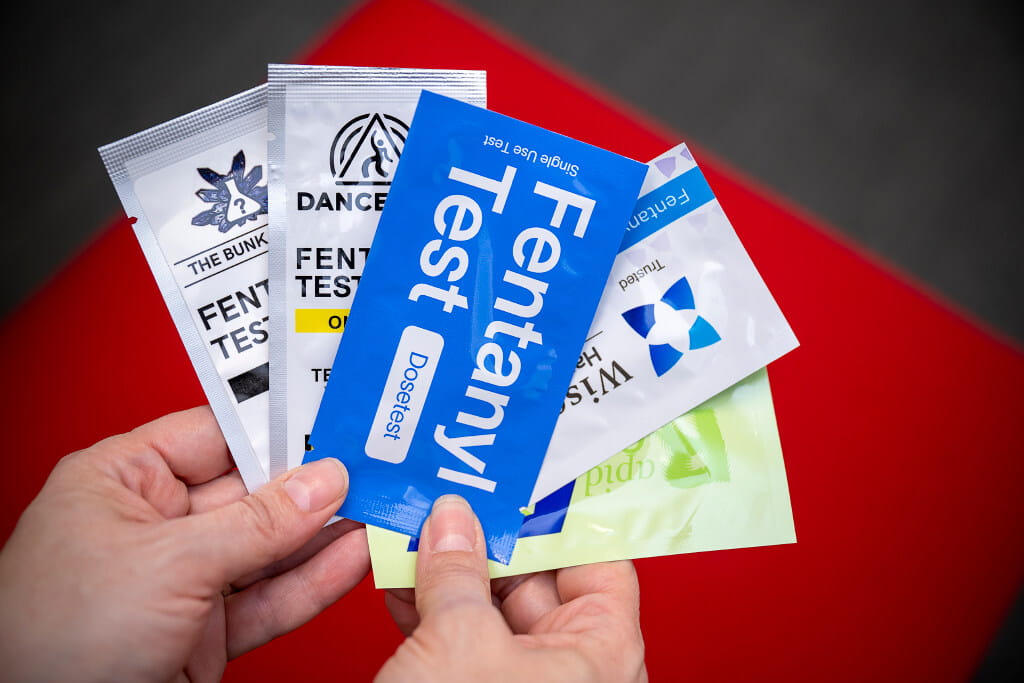 A person's hands hold five different types of Fentanyl Test Strips. 