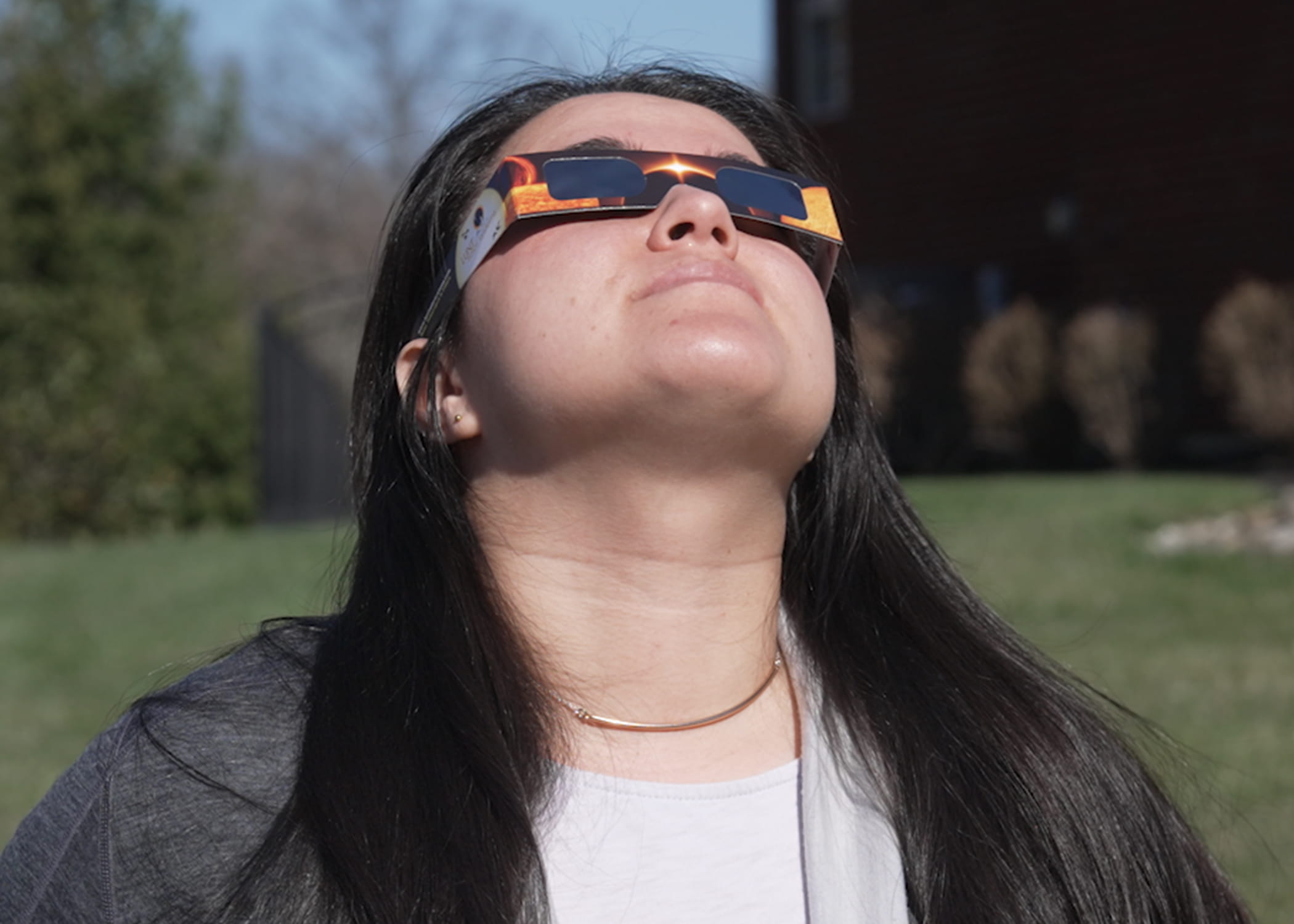 Woman looks at sun while wearing solar eclipse glasses