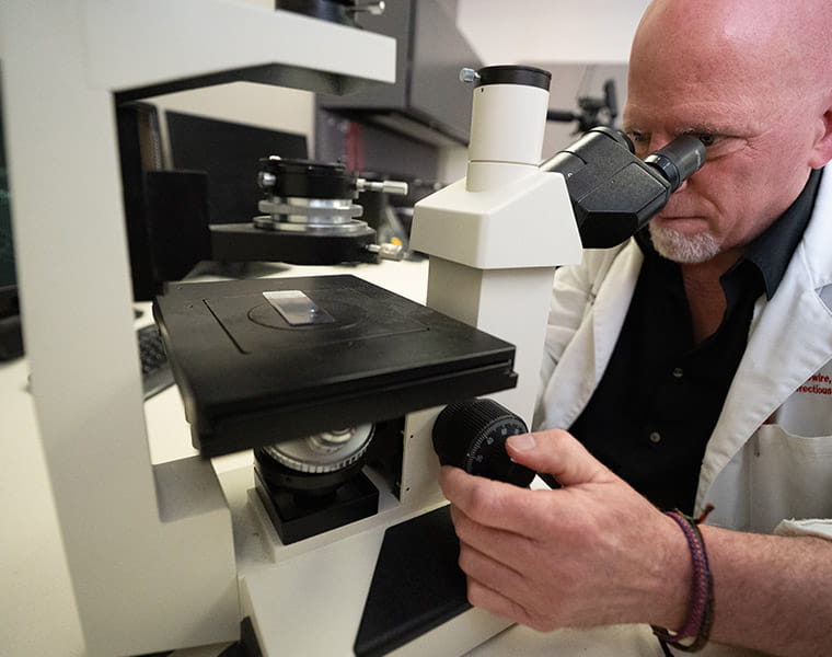 Bradford McGwire, MD, PhD examines leishmania parasites under a microscope. 