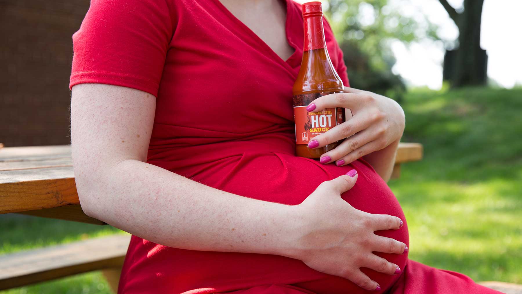 Pregnant woman holding hot sauce bottle to illustrate a common myth to start labor with spicy foods.