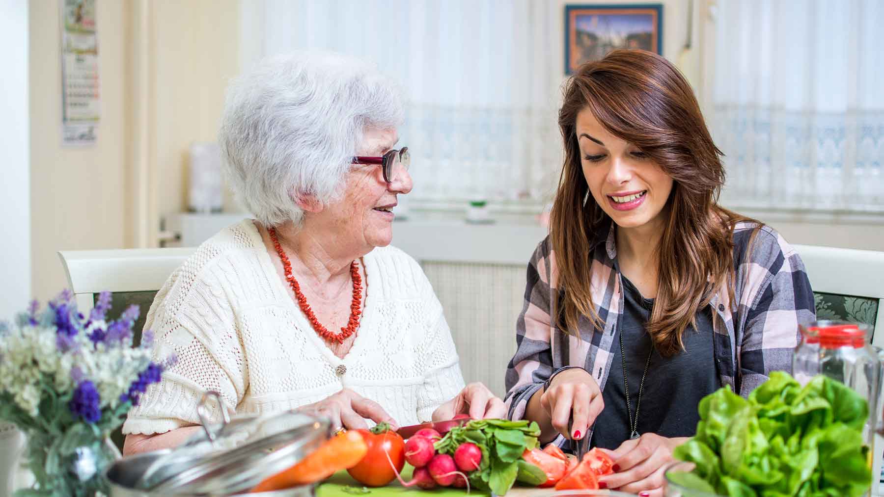 elderly woman and younger woman sitting at table chopping vegetables