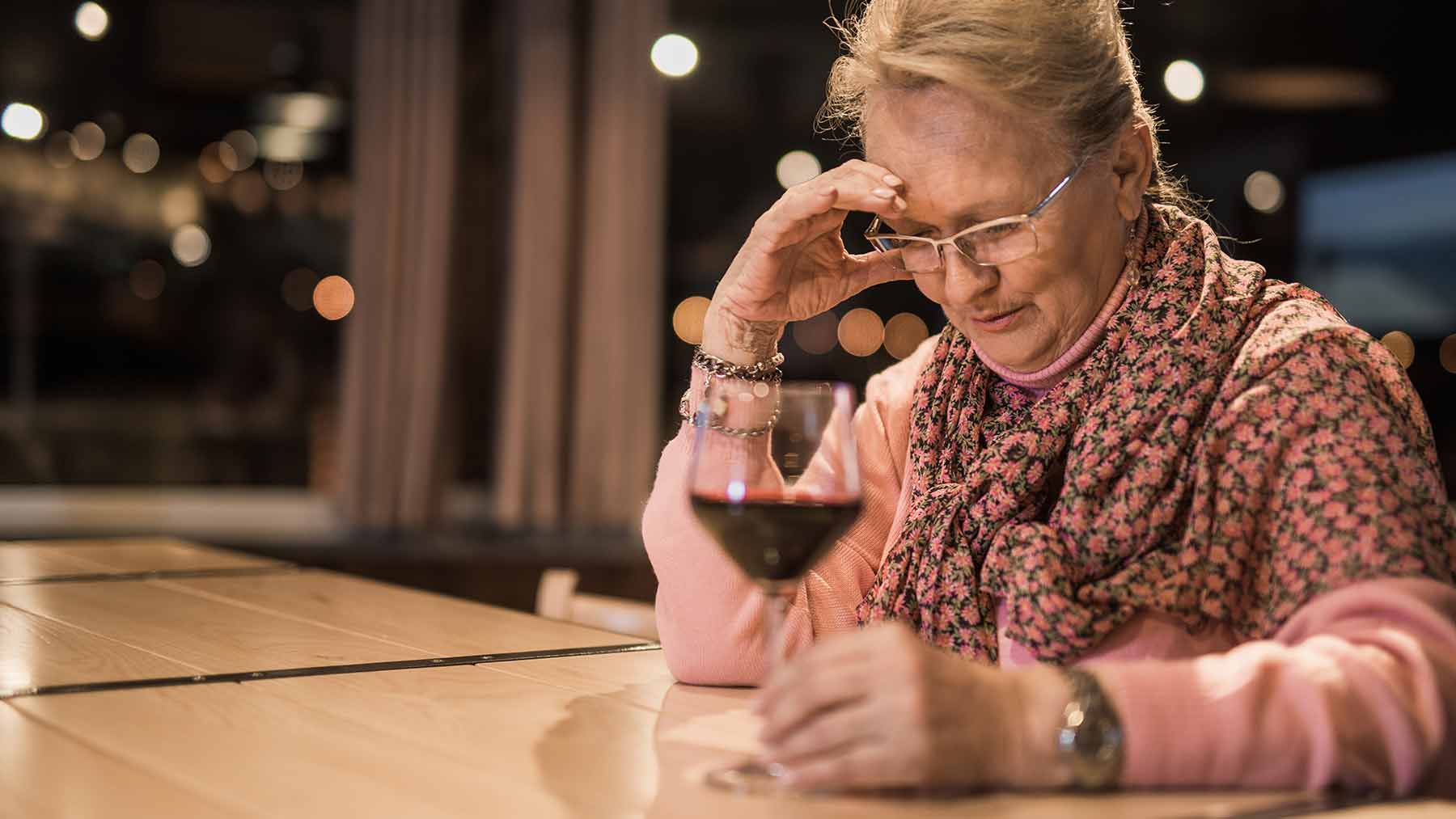 sad, older woman sitting at bar with a drink