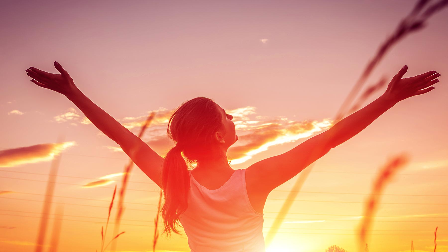 woman holding out arms wide with sunrise behind her
