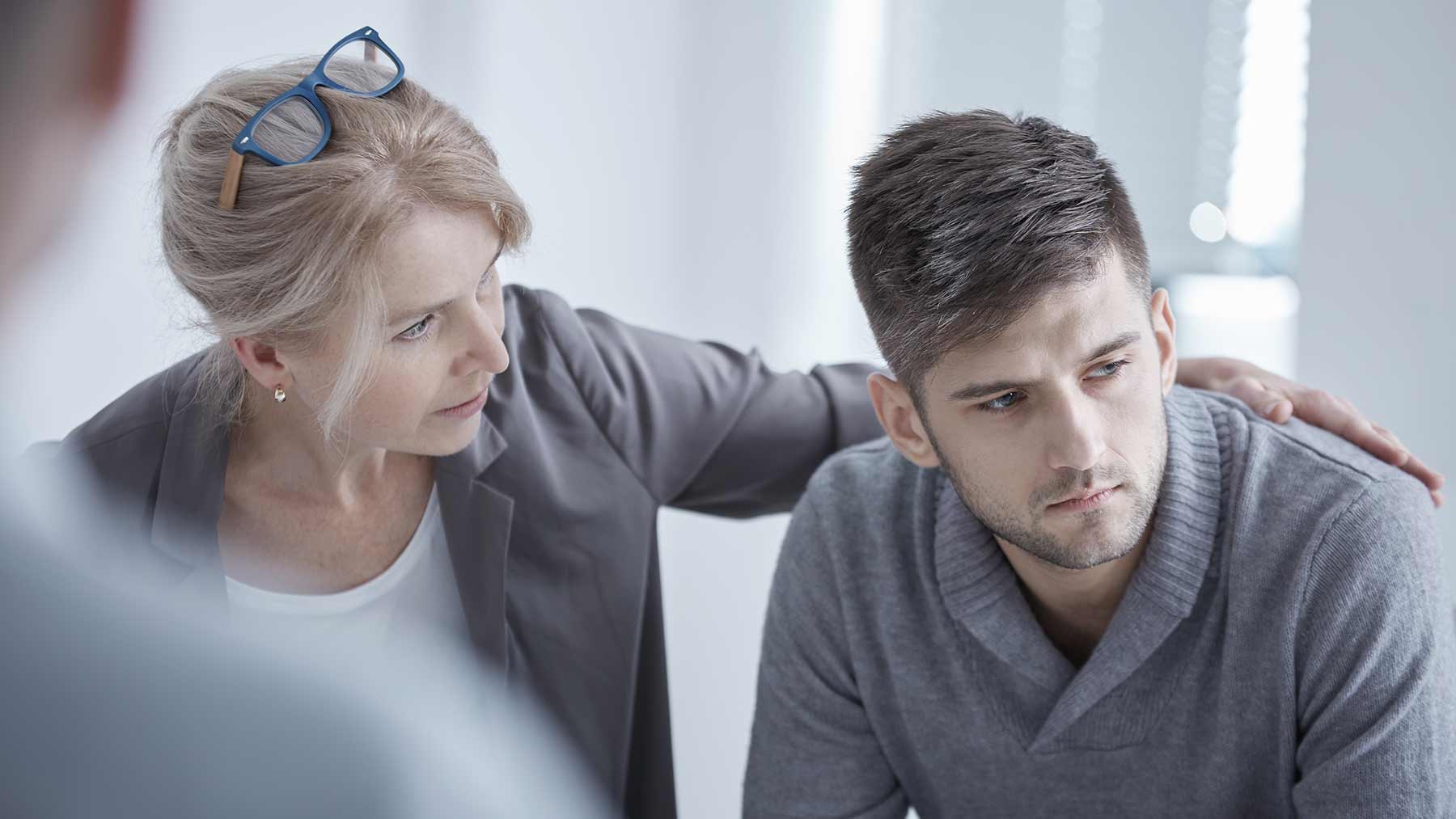 woman puts arm around troubled young man to communicate with him