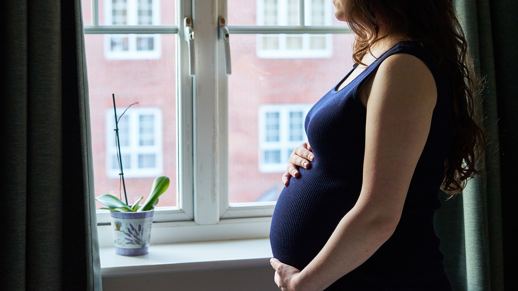 Pregnant woman holds her belly while looking out window