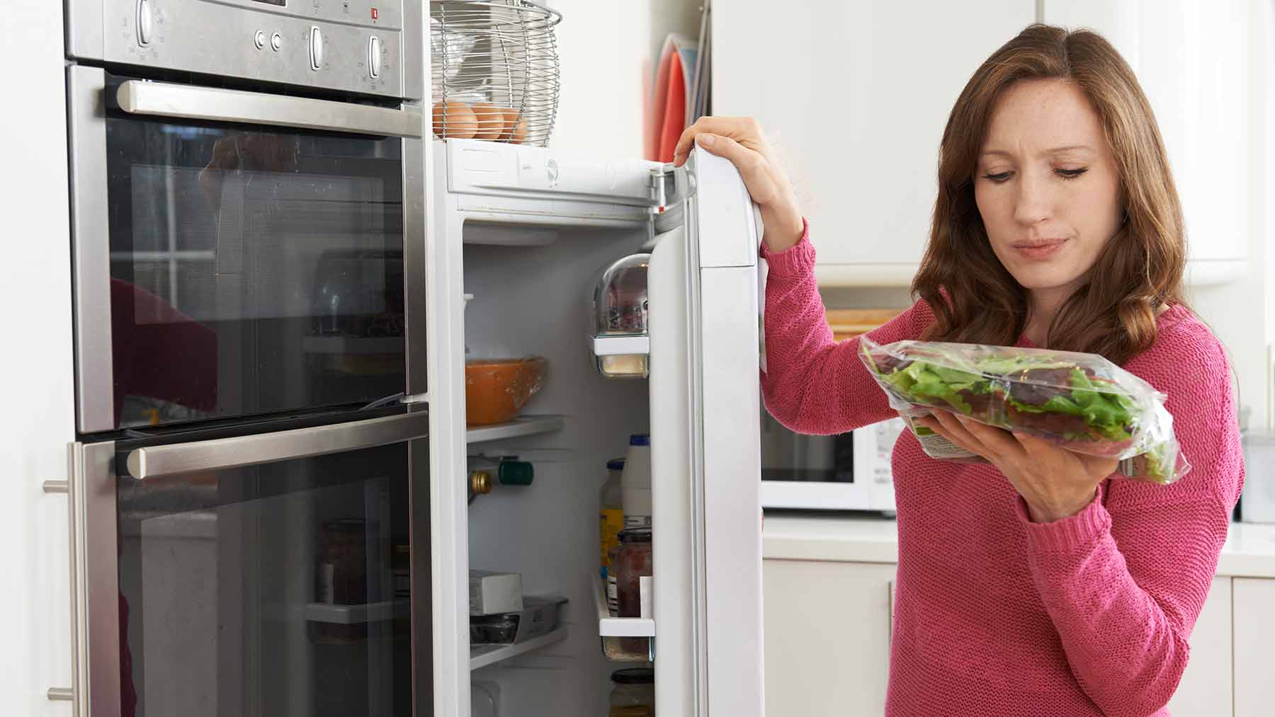 woman looking at food label near open refrigerator
