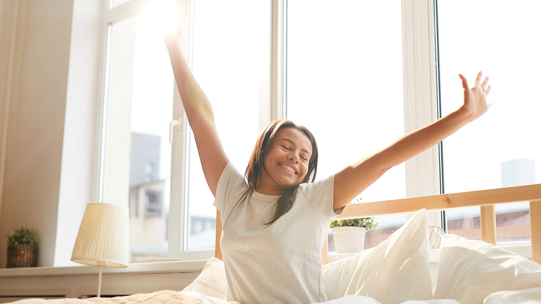 woman stretches arms in bed on sunny day