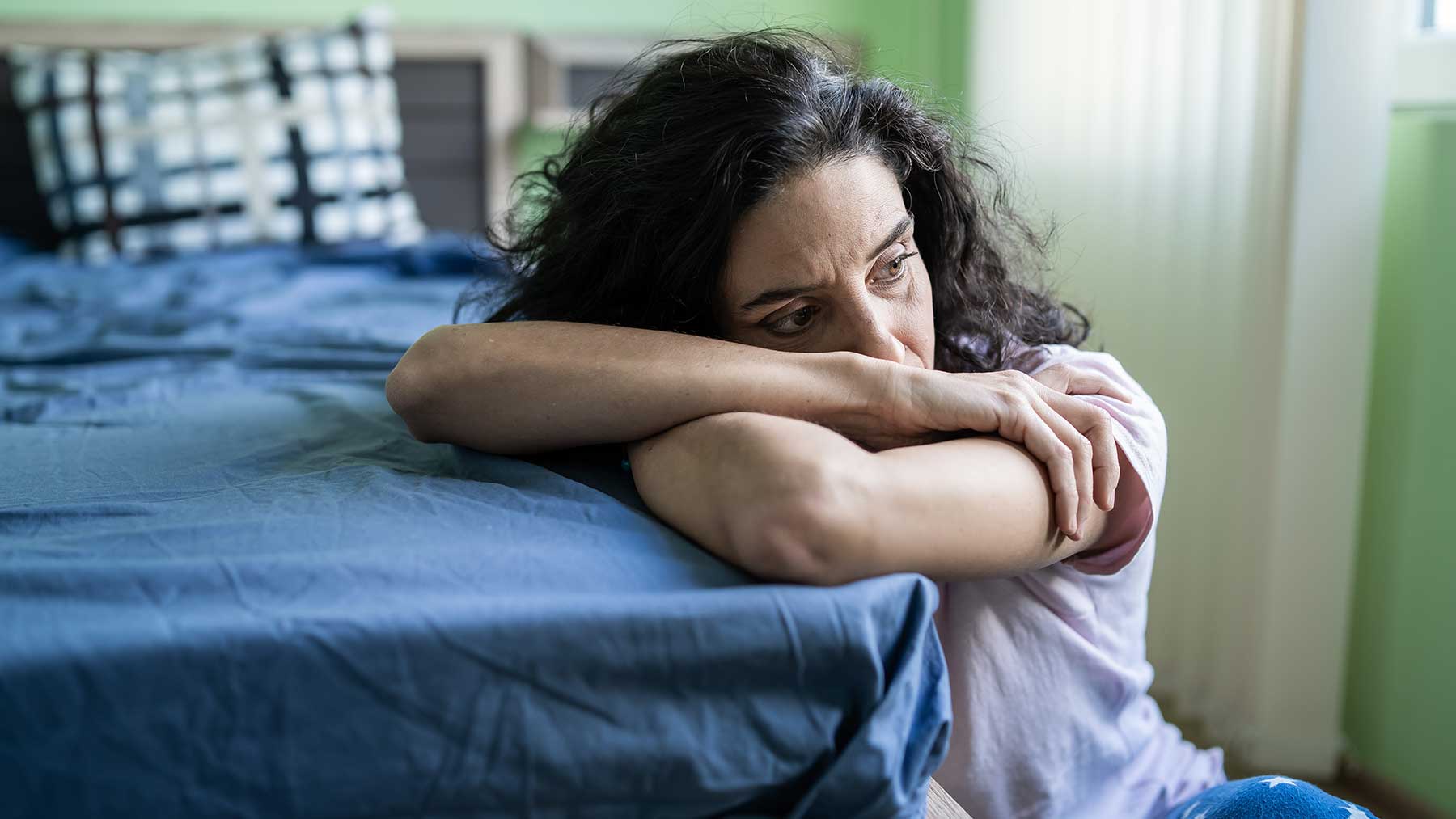 Sad woman sitting on floor leaning on bed