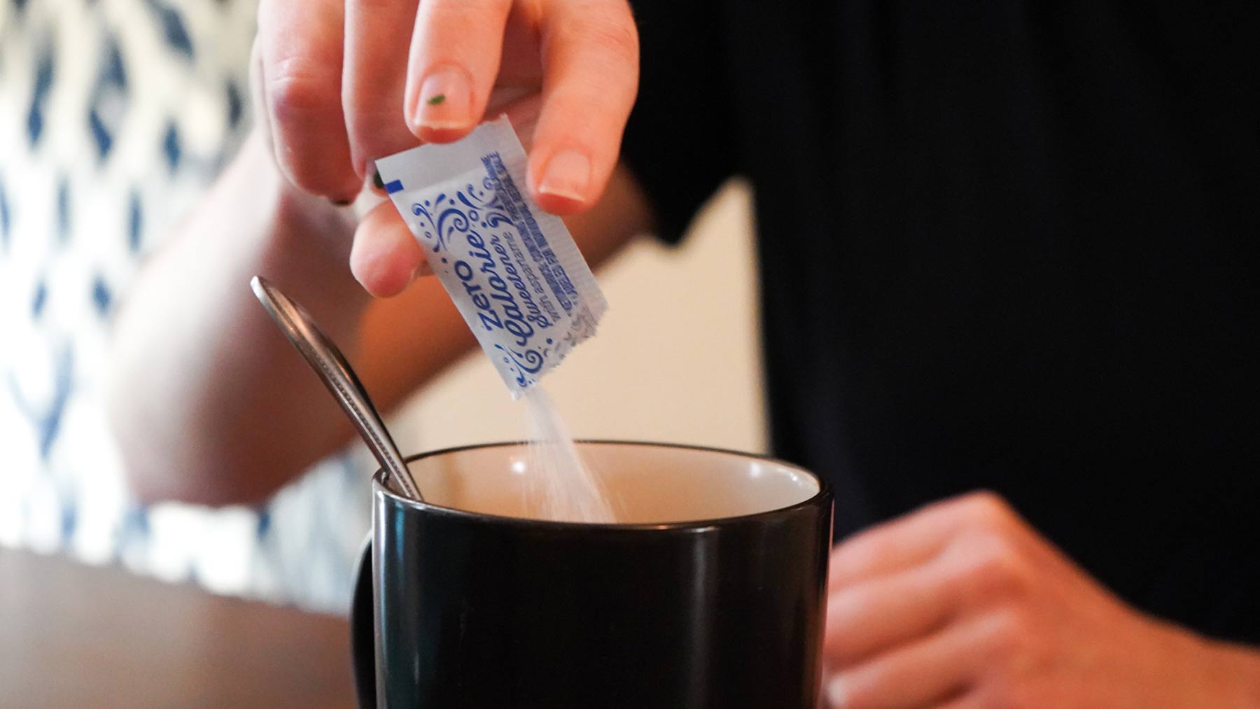 woman adding artificial sweetener to coffee