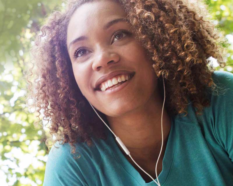 Woman wearing earbuds outside smiling