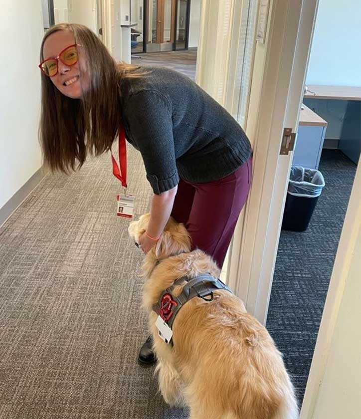 A woman smiles while petting a golden retriever.