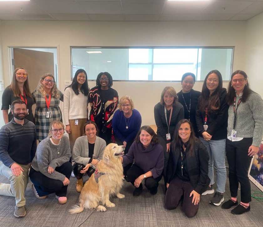 Fourteen CATALYST faculty and staff members pose together around a happy golden retriever.