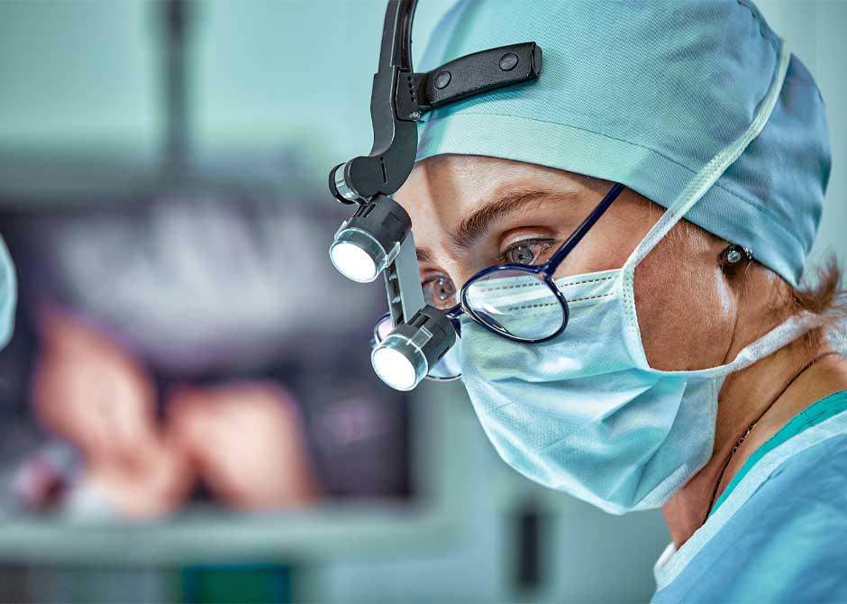 Female surgeon in operating room wearing face mask, glasses and headlamp