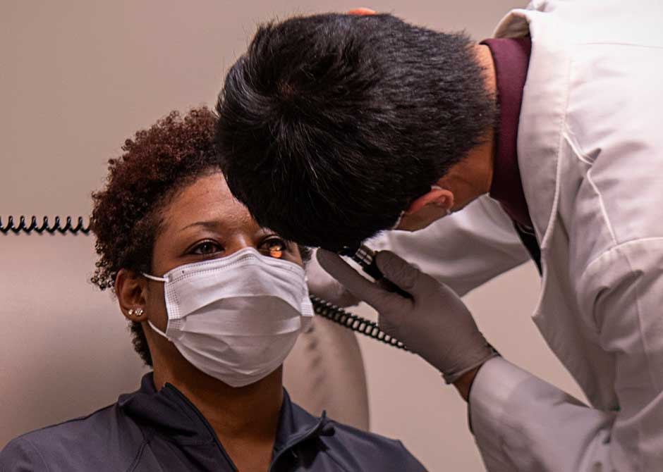 Doctor visually examining the eye of a woman wearing a face mask