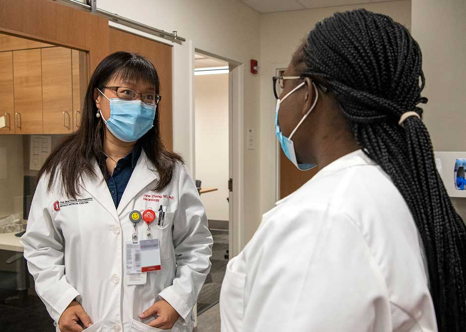 Doctors Moroi and Gyang smiling at one another inside medical office wearing face masks