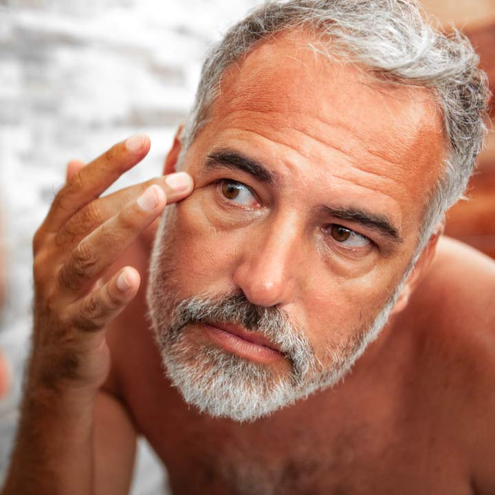 Man with eye bags looking in a mirror