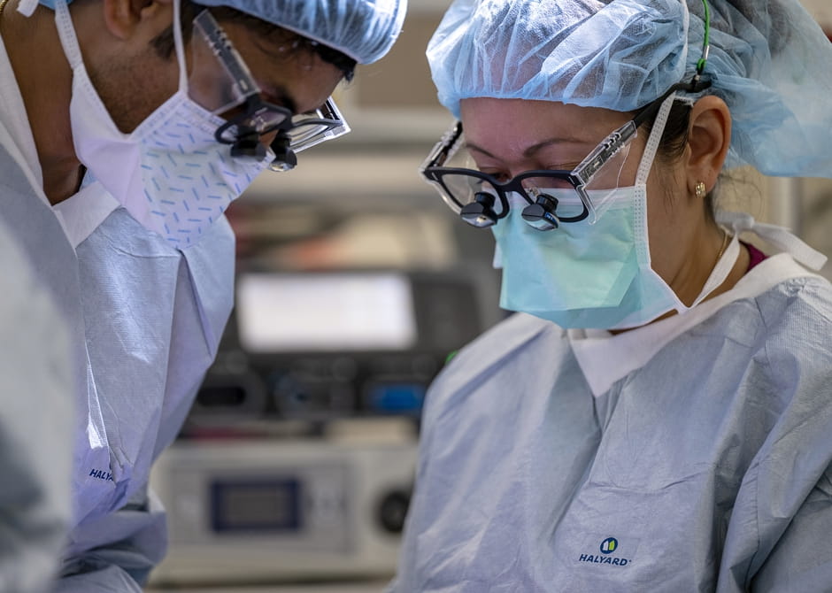 Close-up image of two cardiac surgeons in operating room using microscope glasses to operate