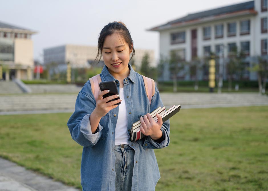 A young college student checks her phone while walking on campus