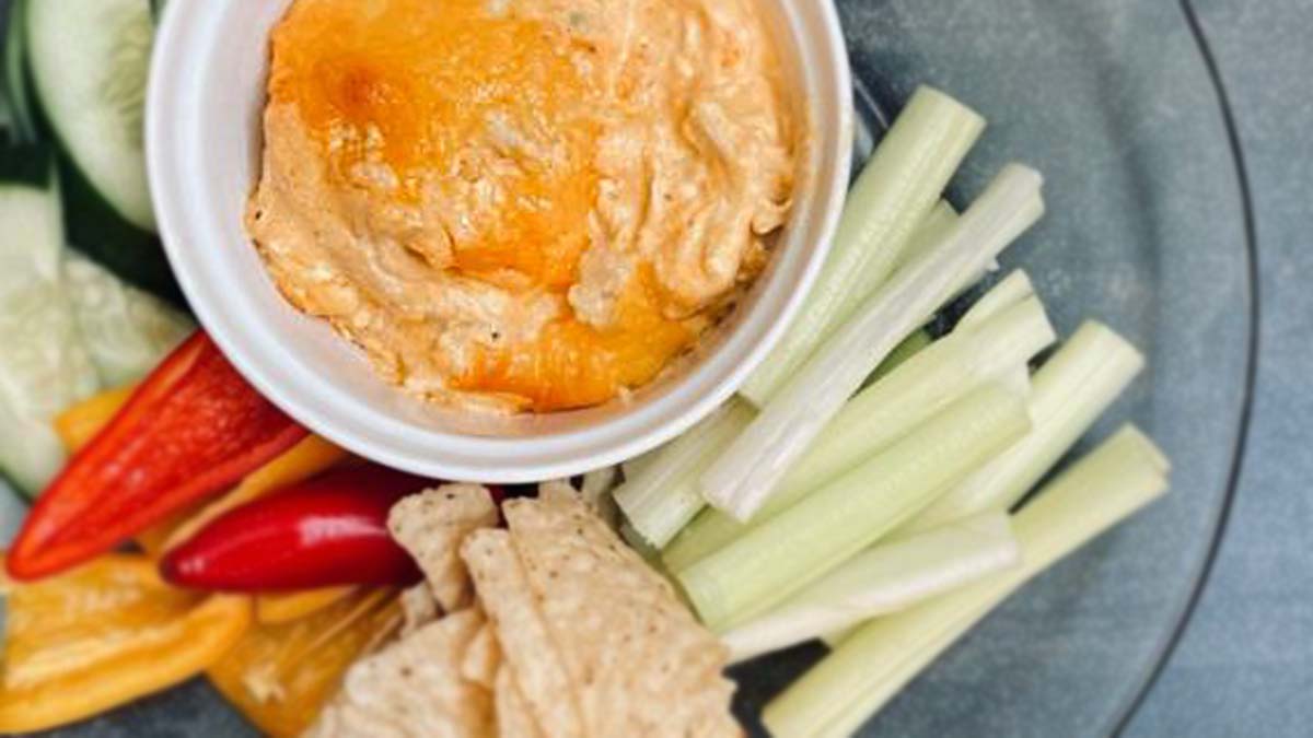 A bowl of buffalo chicken dip surrounded by vegetables and tortilla chips