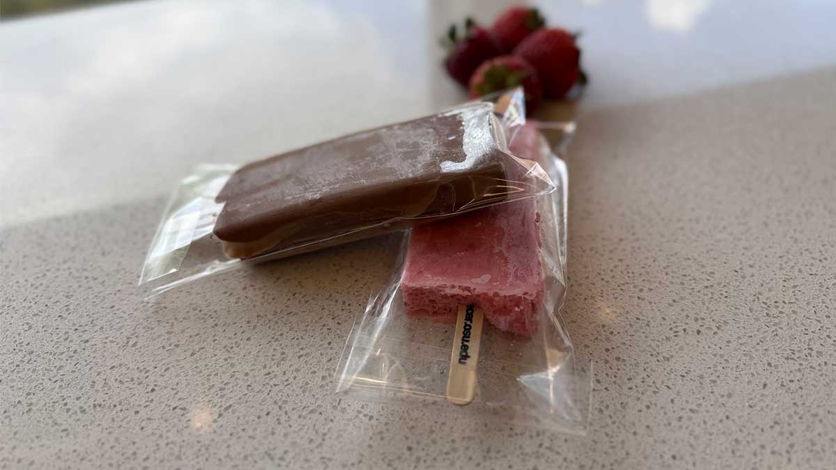 two yogurt popsicles on table with strawberries in the background