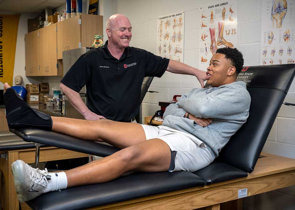 A student-athlete conversing with an Ohio State athletic trainer during a physical