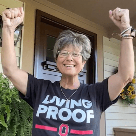 Middle aged female teacher wearing a OSU Living Proof Transplant T-shirt raises arms in celebration