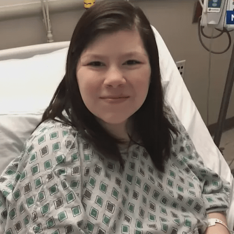 OSU student smiling in hospital bed wearing hospital gown
