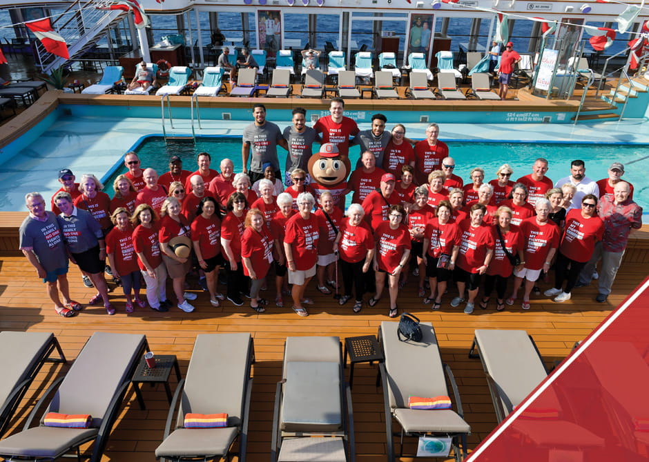 A large group of cruise attendees in matching shirts posing in front of a pool with Brutus Buckeye in the middle